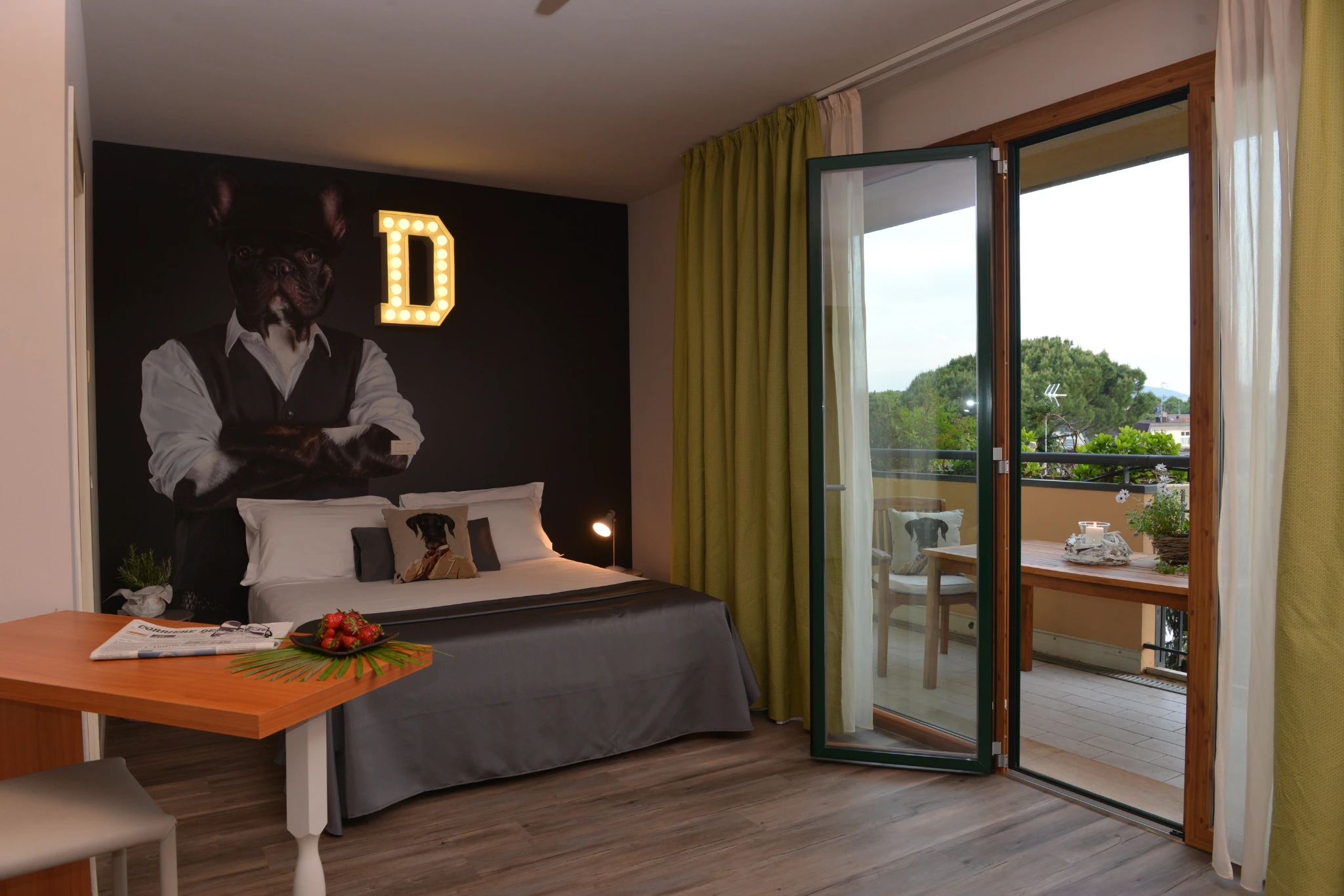 La camera con il murale del bulldog e la D luminosa, e la portafinestra aperta sul terrazzo con il tavolo apparecchiato